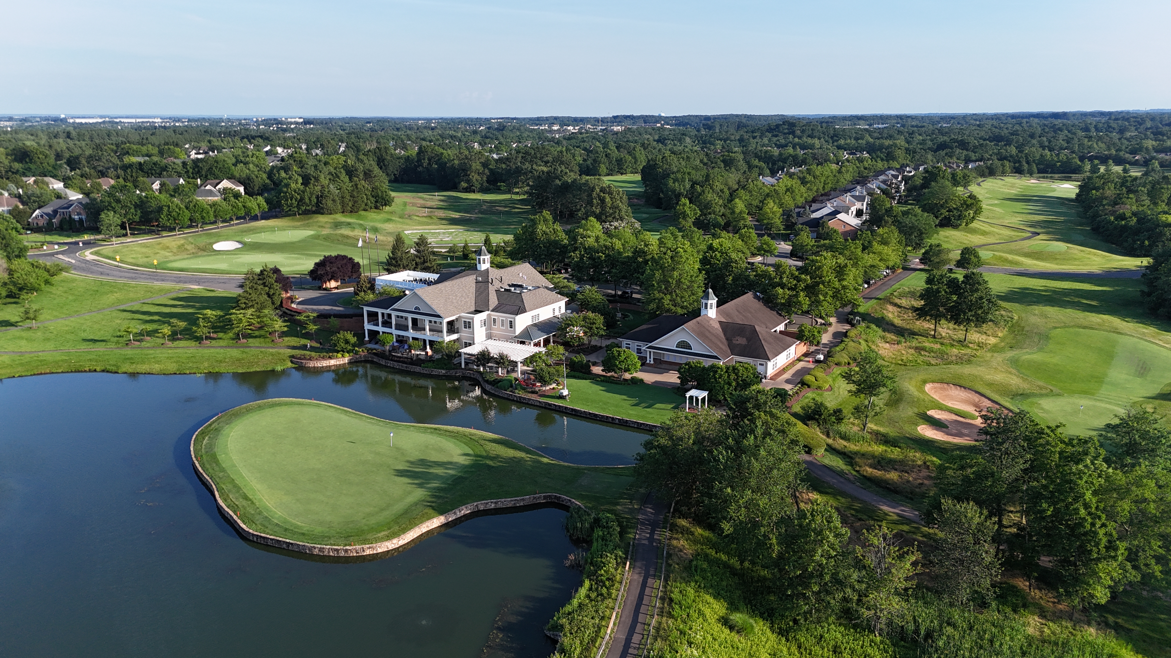 An aerial view of the Dominion Valley Country Club clubhouse and golf course in Haymarket, Virginia, showing the pristine green and a water feature.