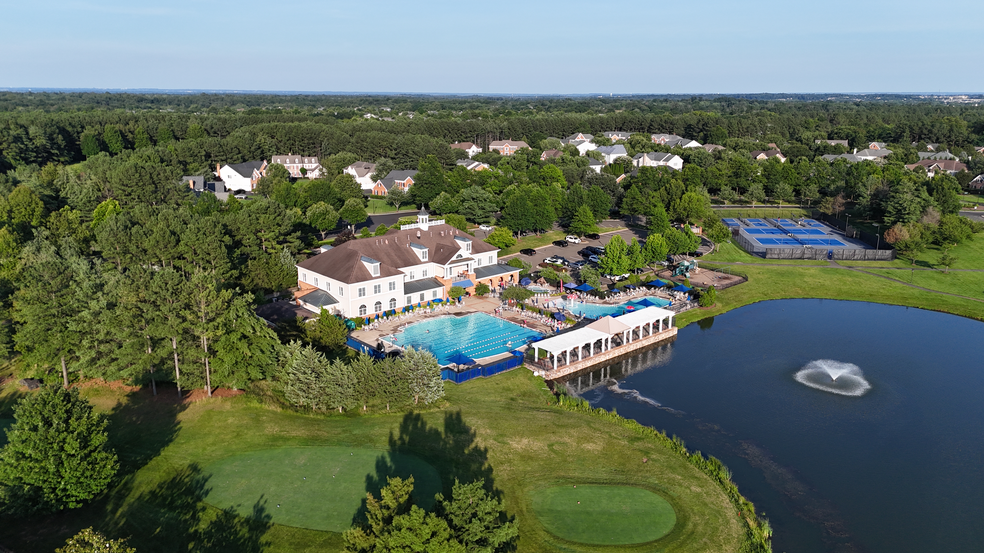 Aerial view of the resort-style amenities at Dominion Valley Country Club, including a large swimming pool, clubhouse, and tennis courts.