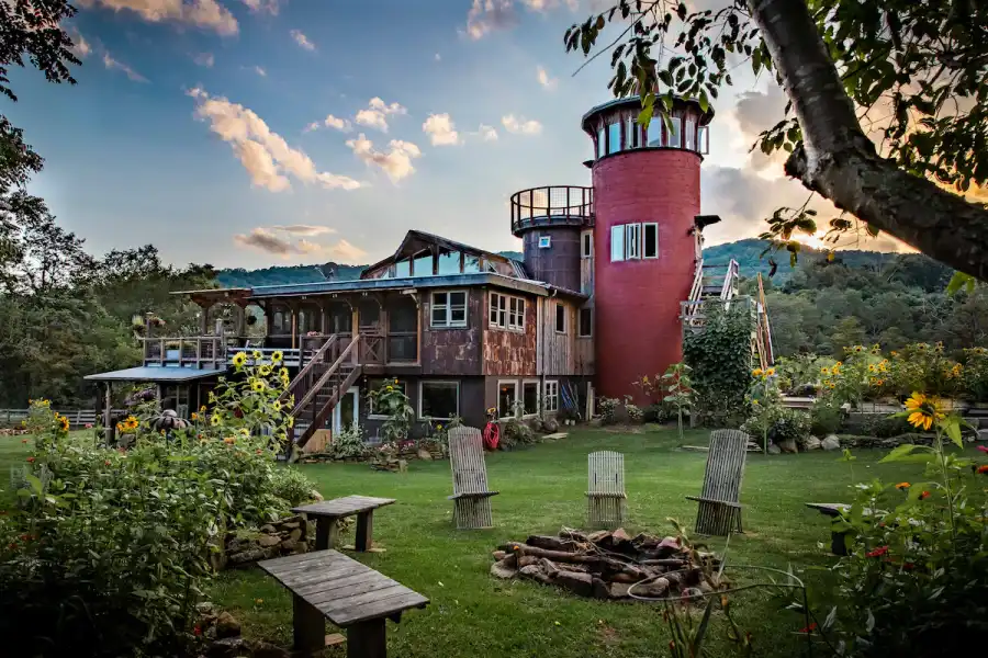 The exterior of the unique Dream Rock Silo Airbnb in Independence, VA, showcasing its red tower, rustic architecture, and surrounding sunflower garden.
