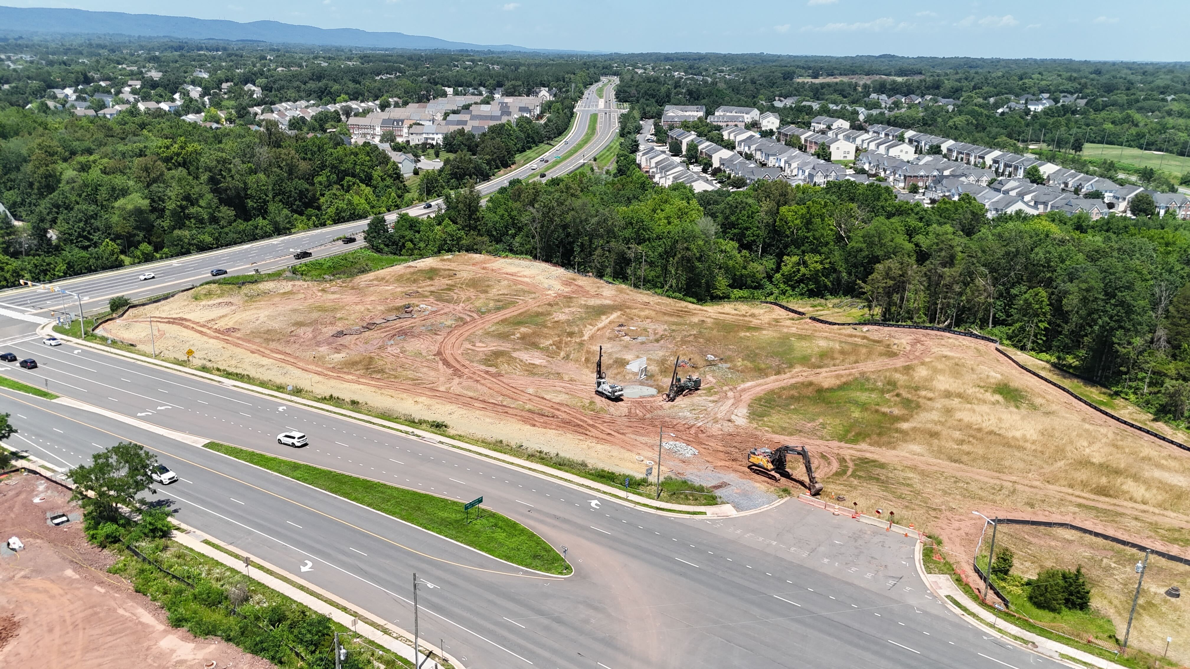 Aerial drone view of a large construction site in Haymarket, Virginia, in the early stages of development, with drilling rigs and an excavator on the cleared land.