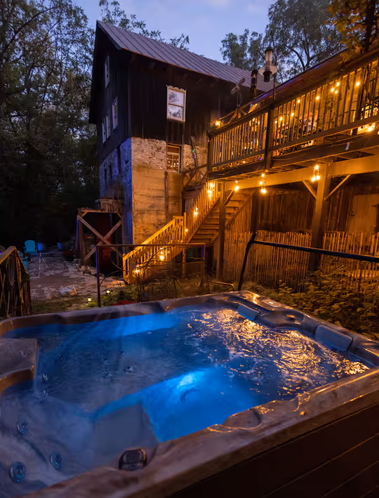 The historic Grist Mill Airbnb in Quicksburg, VA, at twilight, featuring a glowing blue hot tub and warm string lights on the deck.