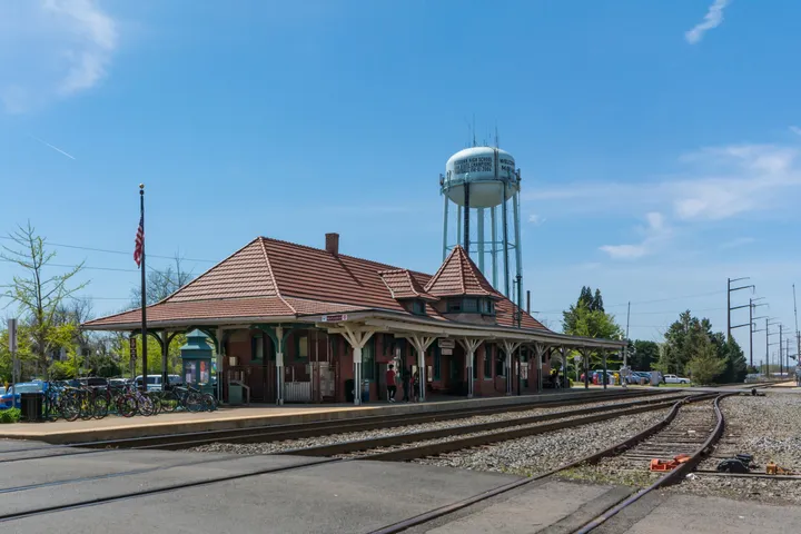 The historic Manassas train station in Virginia, with its brick facade and the city's water tower visible in the background on a sunny day.