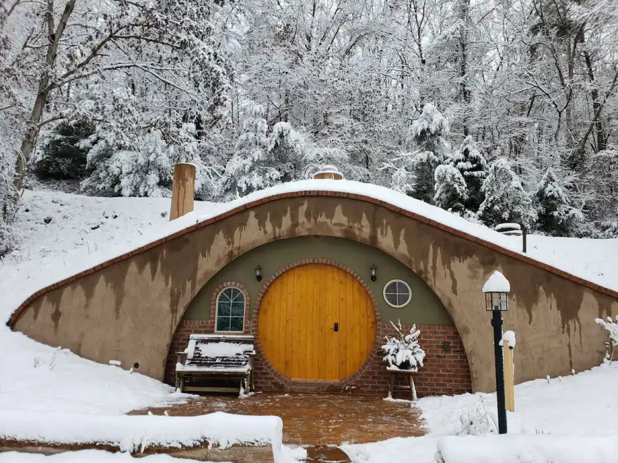 The unique Hobbit Hole style Airbnb in Broadway, Virginia, covered in snow with its bright yellow round door, creating a magical winter scene.