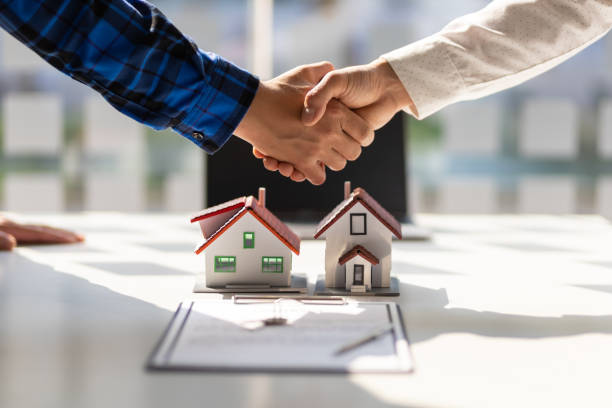 Real estate deal concept with two people shaking hands over a table with model houses and a contract