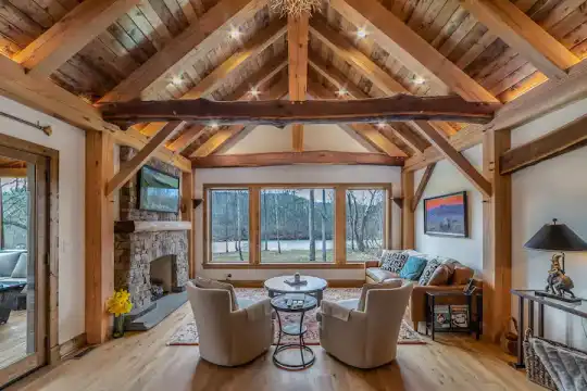 The luxurious timber-frame interior of the Maury River Treehouse in Virginia, featuring a stone fireplace and large windows with a scenic view of the river.