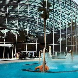 Visitor enjoying thermal bath water features with steam, looking towards the glass exterior of the Therme DC wellness resort.